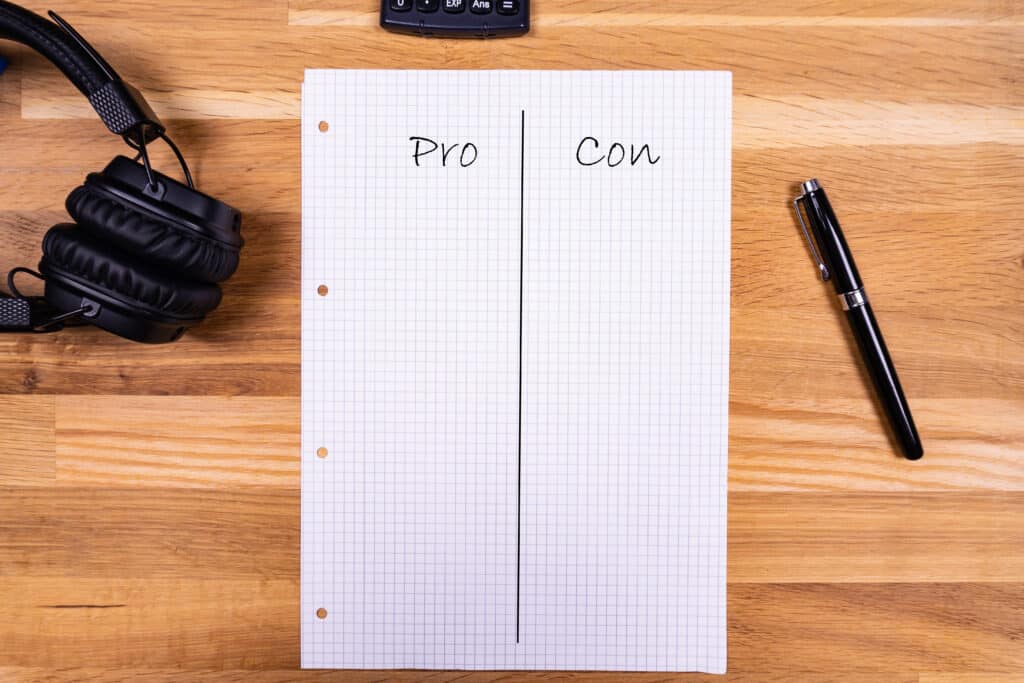 A notepad with a note saying "Pro Con" together with a pen, a ca A notepad with a note saying "Pro Con" together with a pen, a calculator and headphones on a wooden table - flat lay