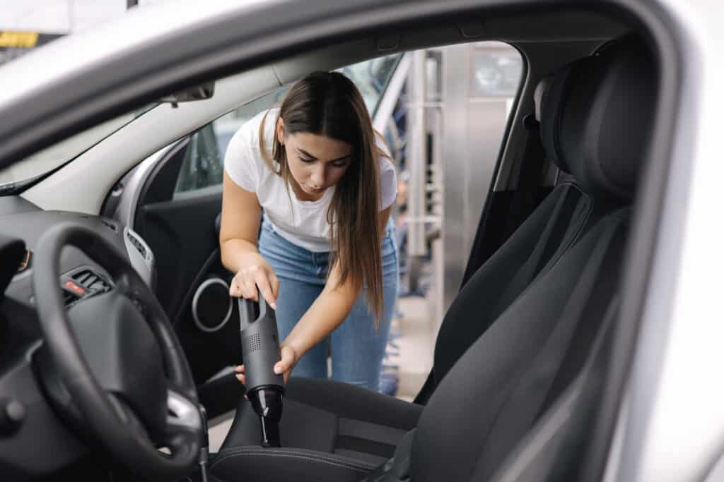 Female using portable vacuum cleaner in her car. Electrical vacuum in woman's hand clean car inside from dust. Self servise car wash Woman using portable car vacuum