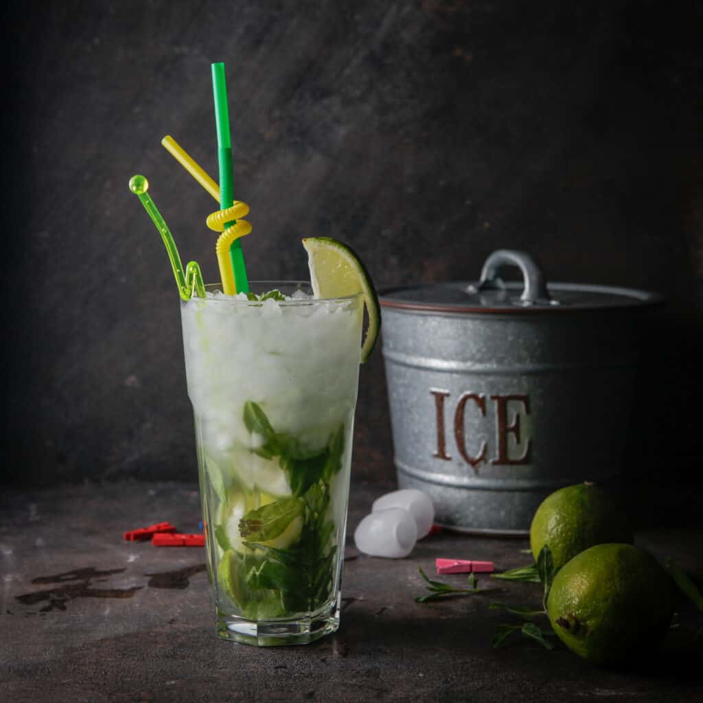 Side view mojito cocktail with mint, lime, ice, ice bucket on a dark background 1 Ice in glass with limes and ice bucket
