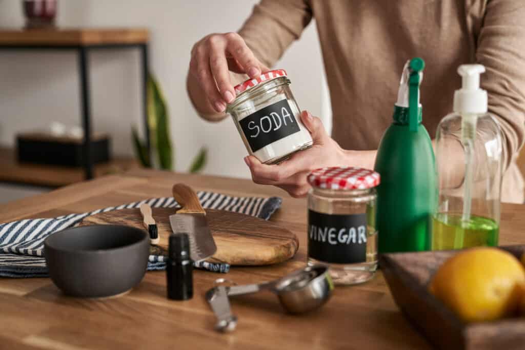 Person mixing home cleaning solution with baking soda, vinegar, and lemon