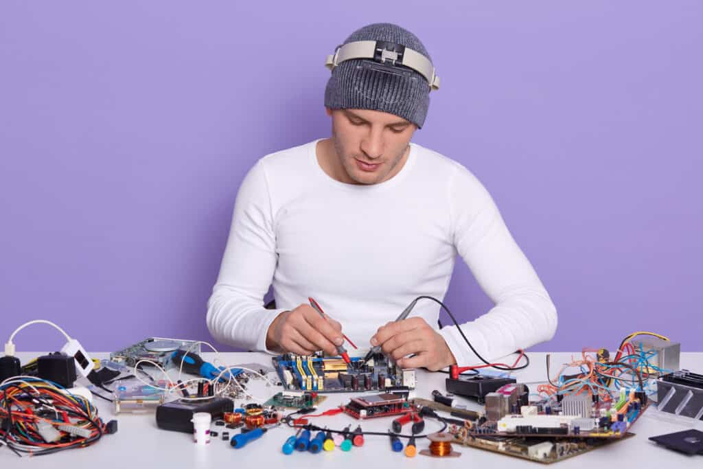 Concentrated technician repairing inside of smartphone or lap top by multimeter in lab, fixing electronic components. Computer hardware, mobile phone, electronic, repairing and upgrade concept.